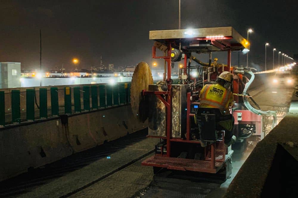 Man using a large industrial concrete sawing cutting tool to do roadside repair work